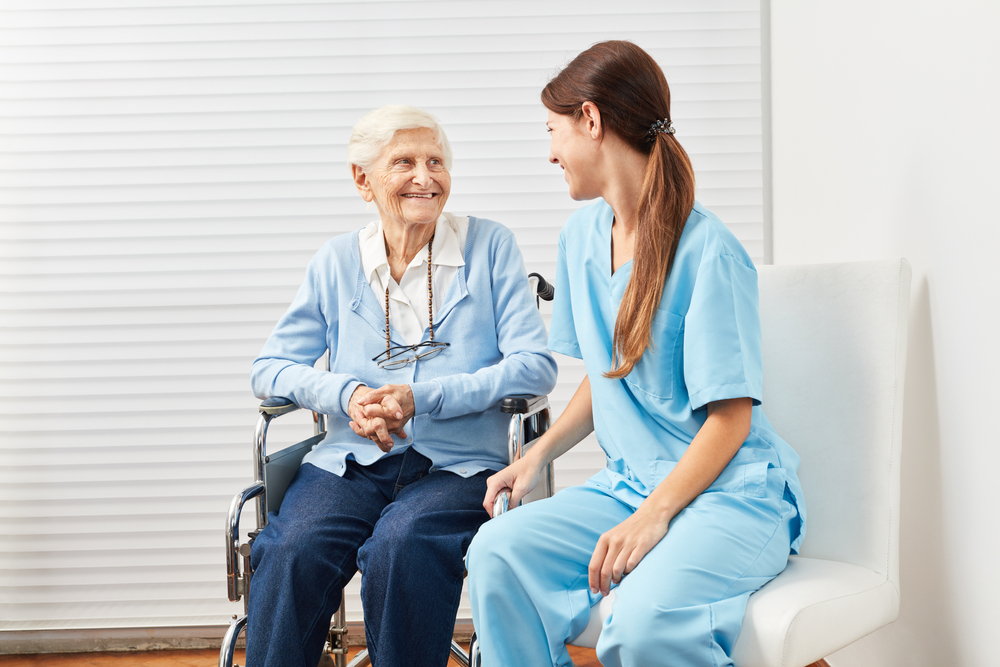 Old senior woman in a wheelchair with a nurse at home nursing